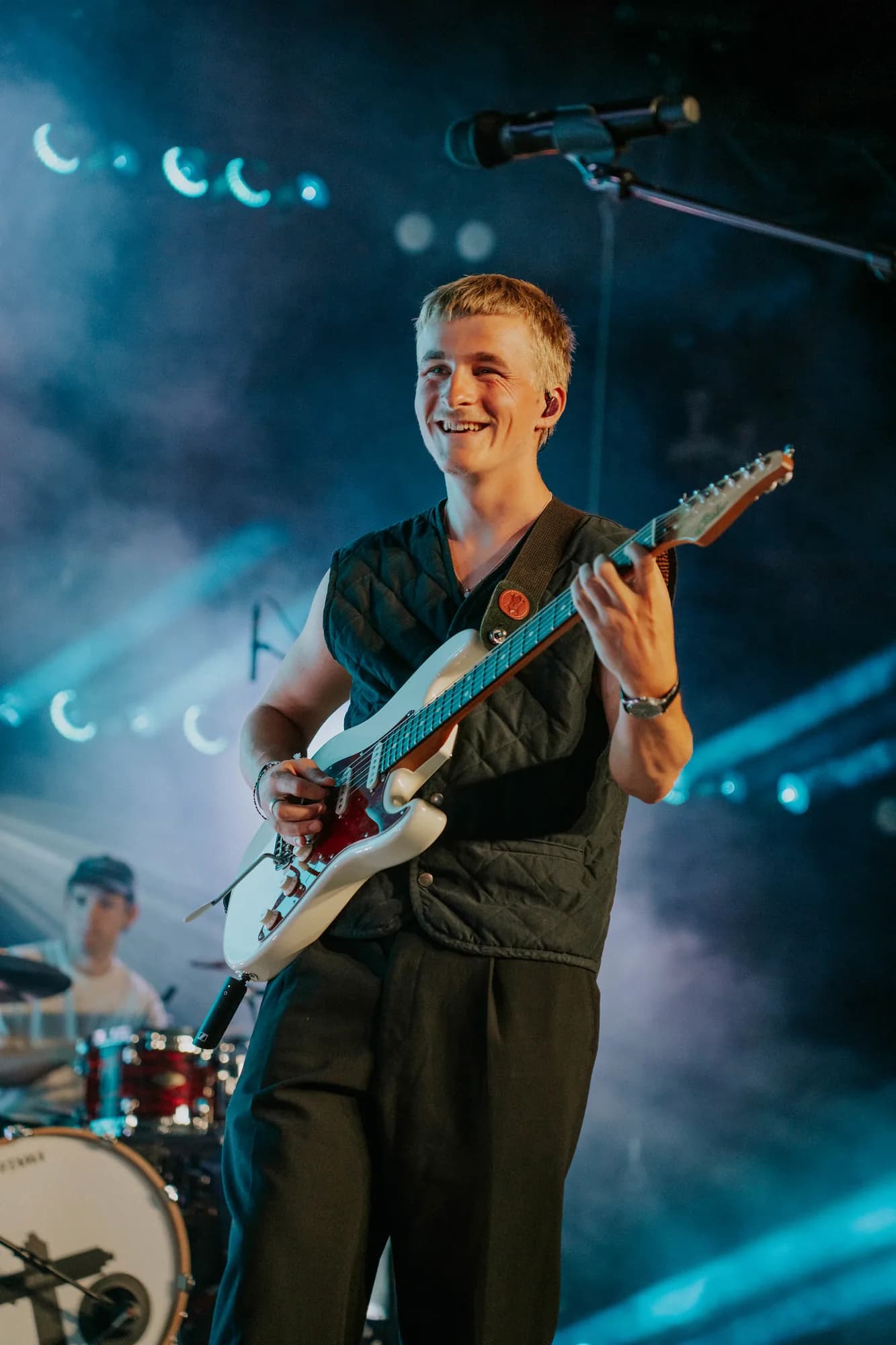 Paloma guitarist smiling on stage in blue light and haze