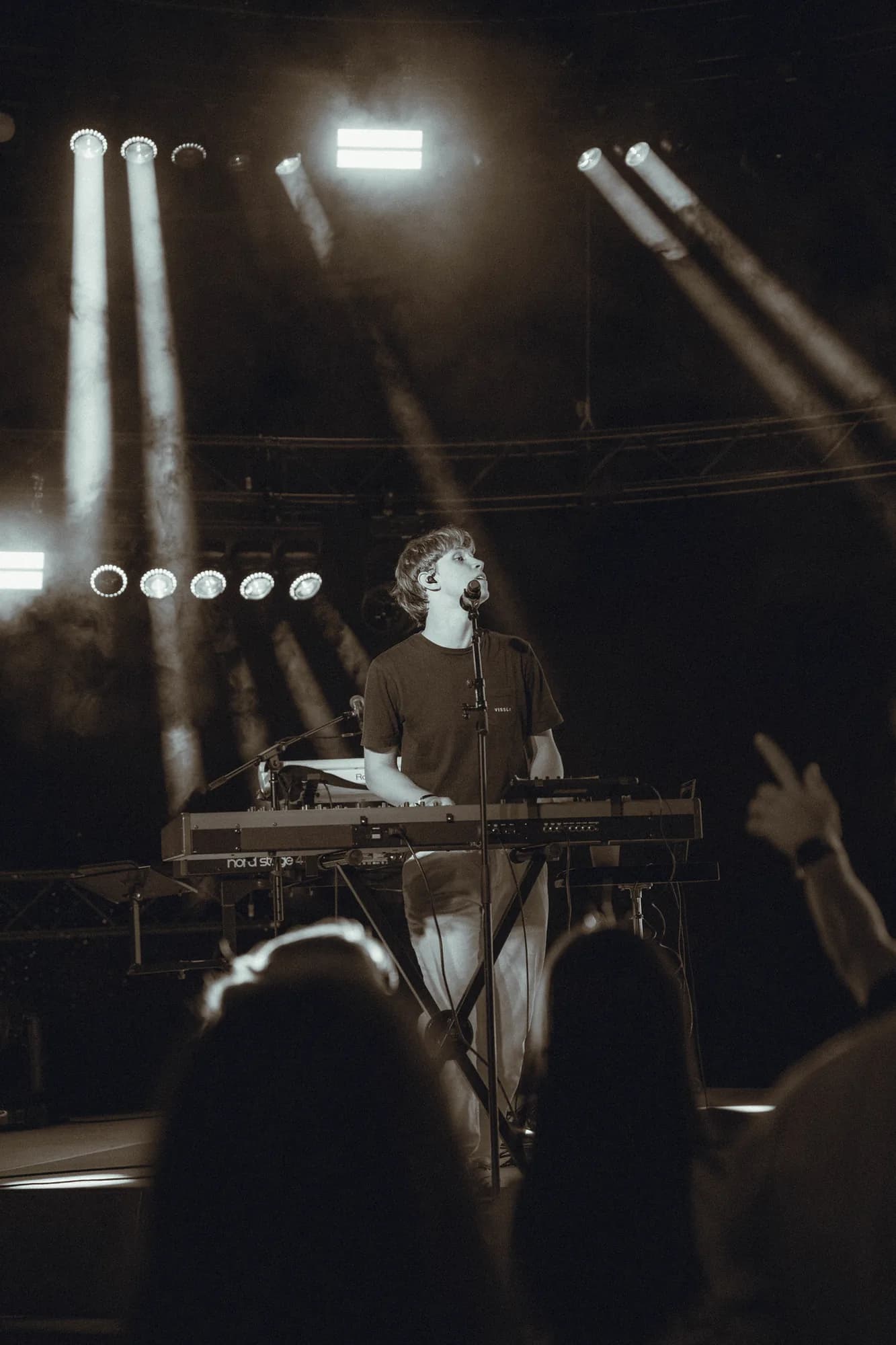 Paloma keyboarder under white beams, hands raised in the crowd